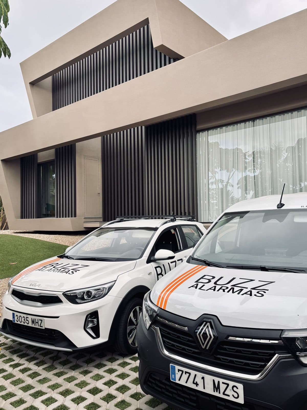 Two Buzz Alarmas vehicles parked outside a modern villa.