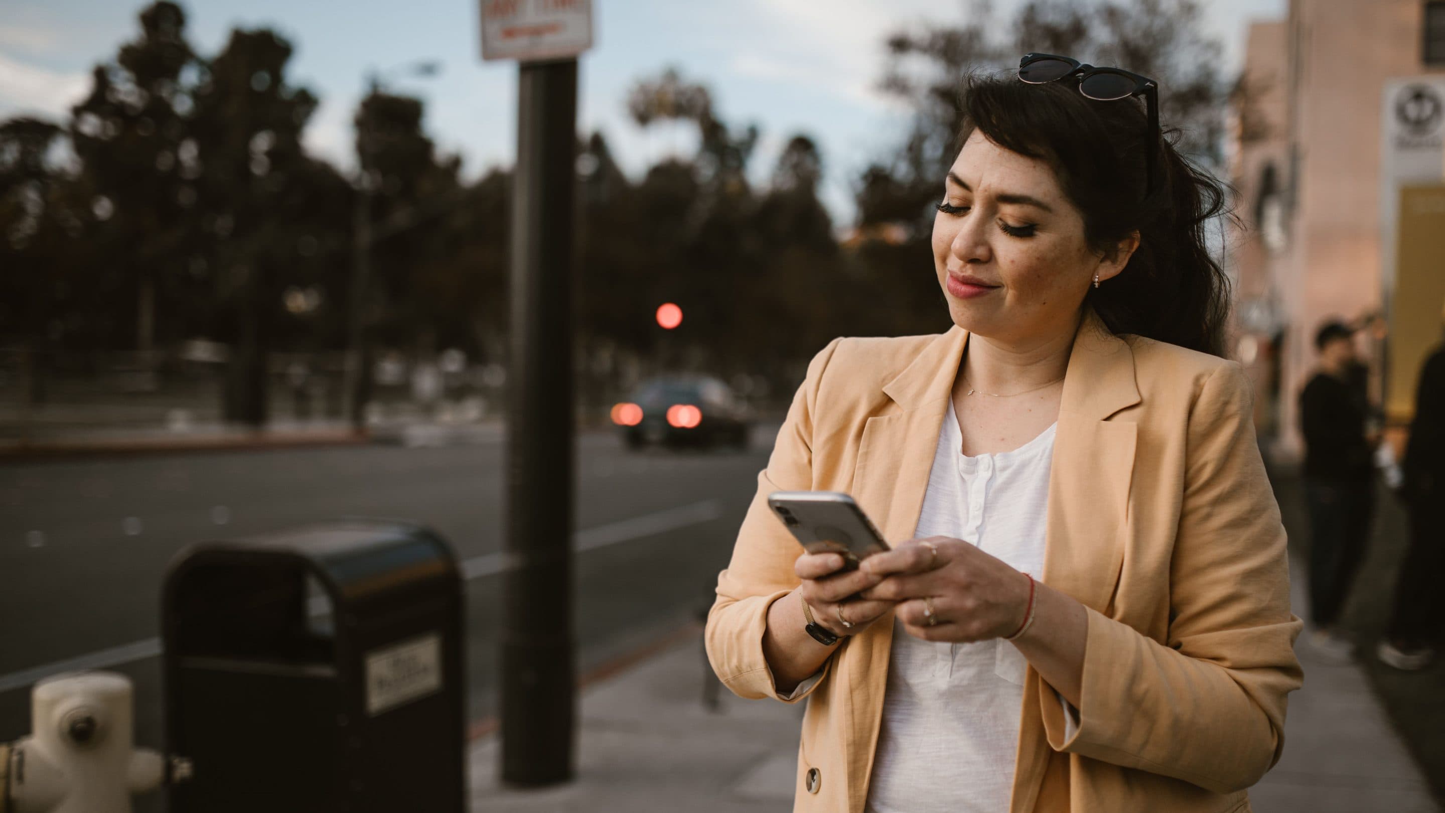 A woman on a city street, reading a customer message on her phone.